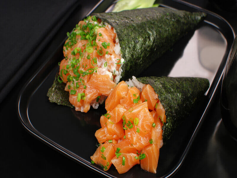 Dois temaki em cima de um prato preto decorado com salsinha e cebolinha picada