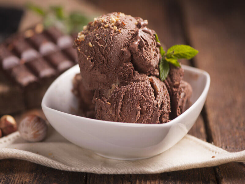 Recipiente branco com duas bolas de sorvete de chocolate polvilhado com avelã triturada e decorado com folhas de hortelã