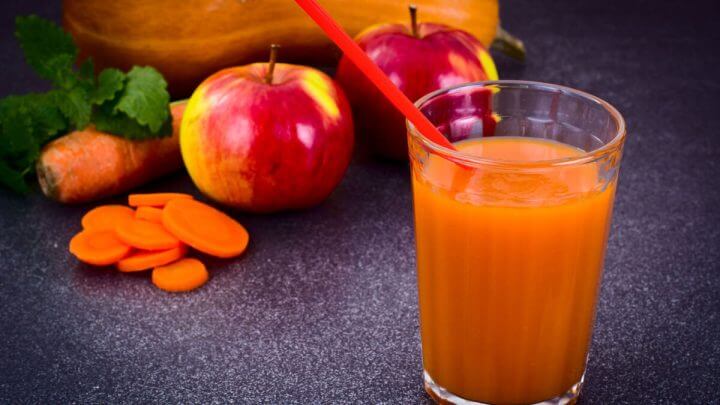 Suco de cenoura no copo com canudo vermelho e maçã e cenouras cortadas ao fundo