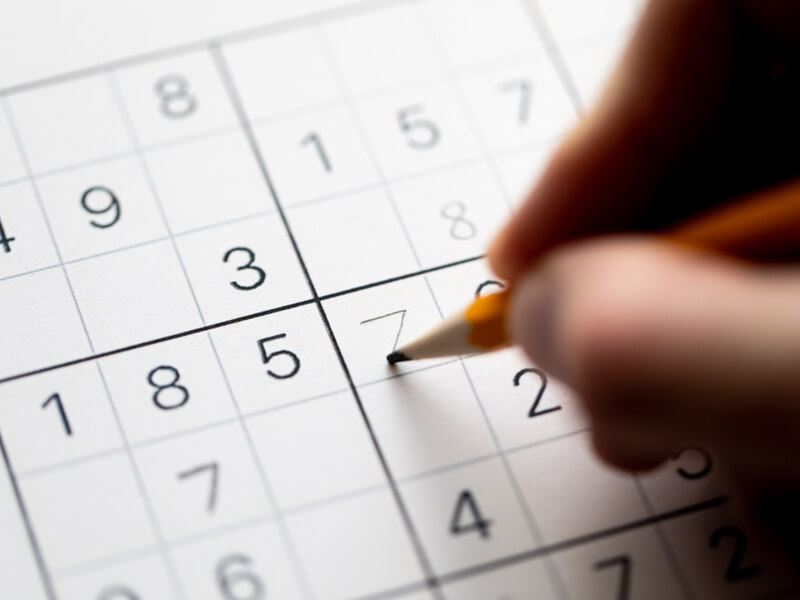 Close em uma mão segurando um lápis e jogando sudoku