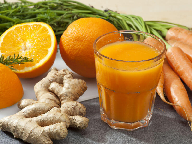 Suco de cenoura com laranja em copo de vidro e gengibre, lnranja e cenoura ao lado do copo