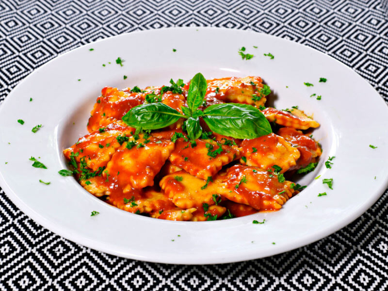 Ravióli com molho de tomate e manjericão em prato branco
