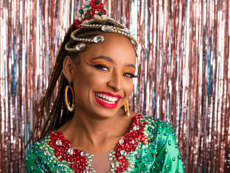 Mulher maquiada com adereços de pedras na cabeça, brincos grandes e roupa com pedras brilhantes