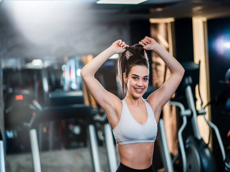 Mulher em uma academia mexendo no cabelo