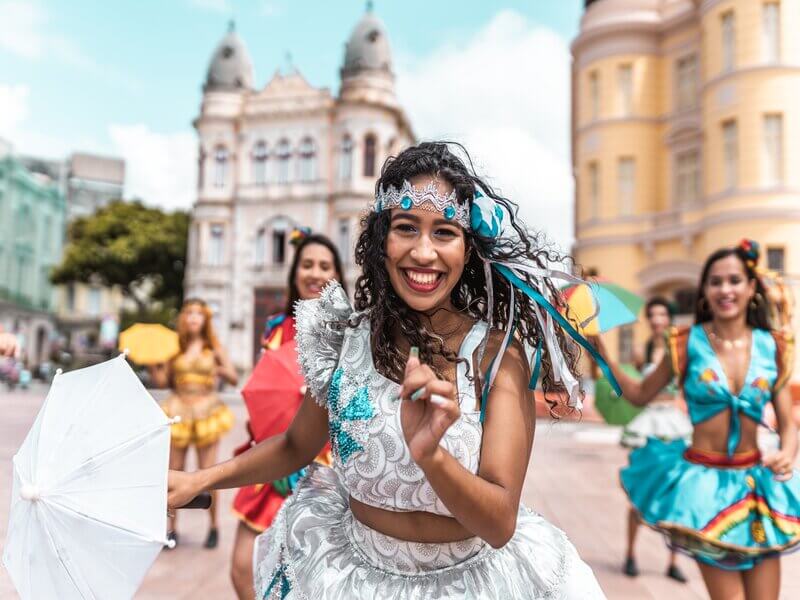 Mulher de blusa e saia branca com tiara azul dançando frevo
