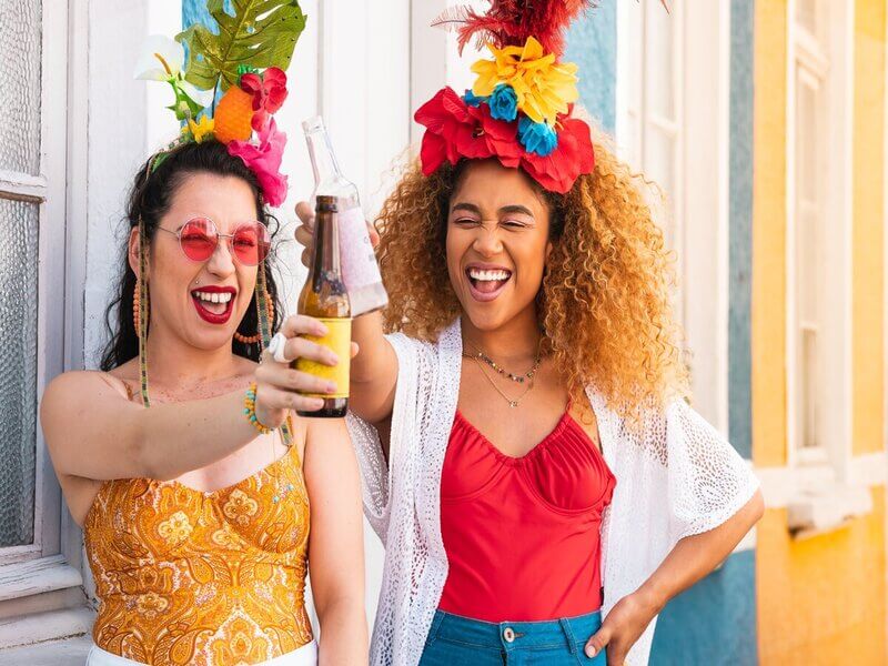Duas mulheres com roupa de carnaval e brindando com garrafa de bebida