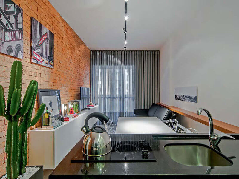 Sala de estar com parede laranja e sofá preto integrada com cozinha