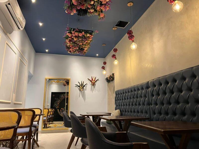 Ambiente decorado com cadeiras e estofado escuro, paredes cinza e flores no teto