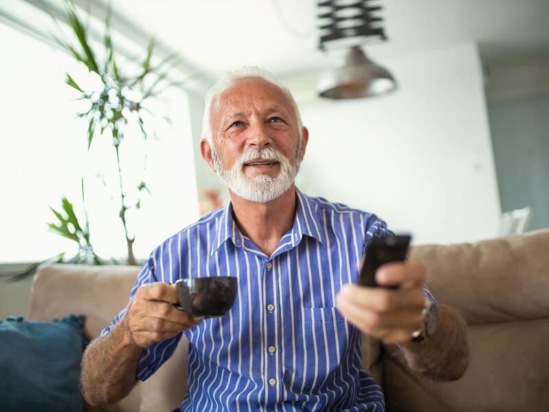 Senhor assistindo televisão e segurando xícara de café
