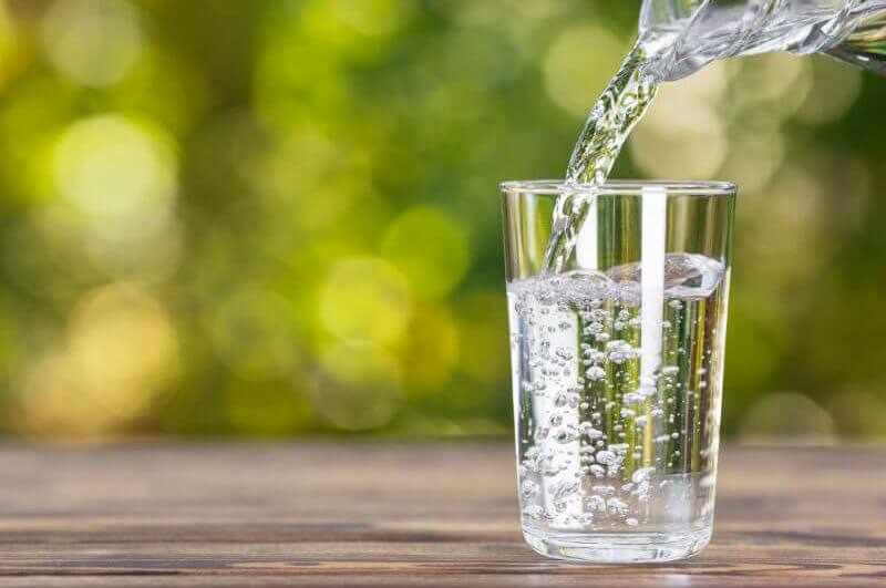 Água do jarro sendo despejada em vidro na mesa de madeira ao ar livre