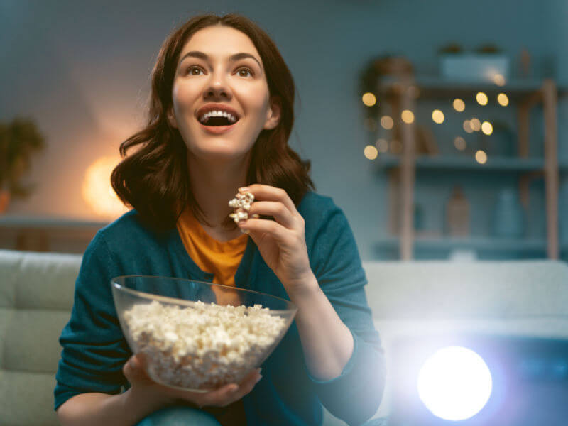 Jovem mulher assistindo projetor, TV, filmes com pipoca à noite. Garota passando um tempo em casa.