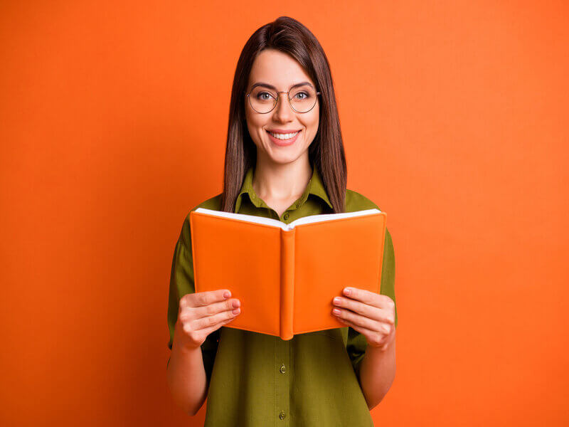 Mulher de blusa verde sorrindo segurando um livro