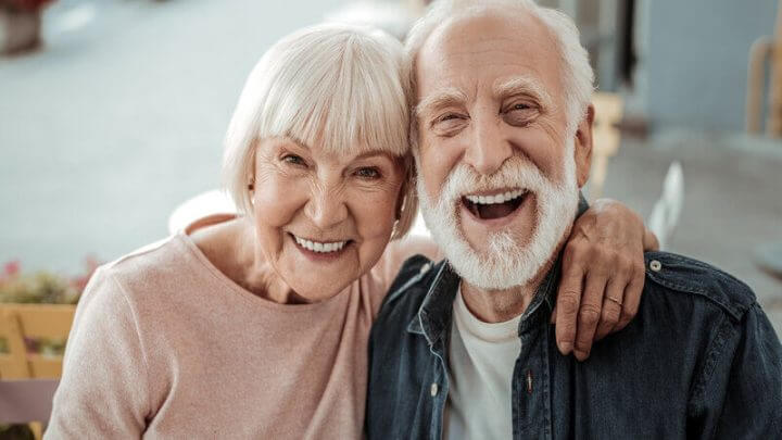 Mulher e homem idosos com a cabeça apoiada um no outro e sorrindo