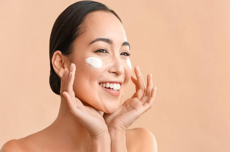 Mulher sorrindo passando creme no rosto