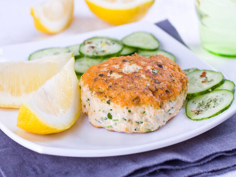 Prato branco com hambúrguer de salmão, rodelas de pepino e limão