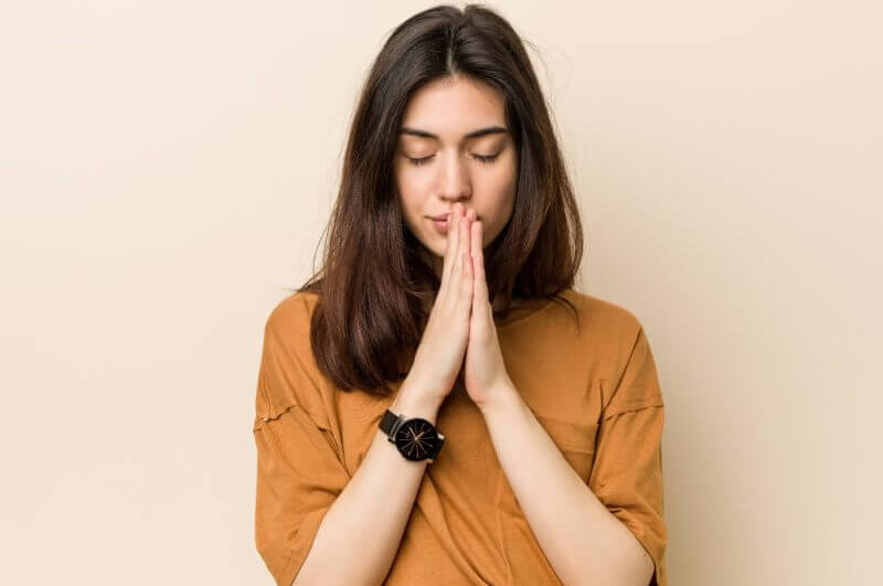 Mulher com camiseta marrom, olhos fechados e rezando