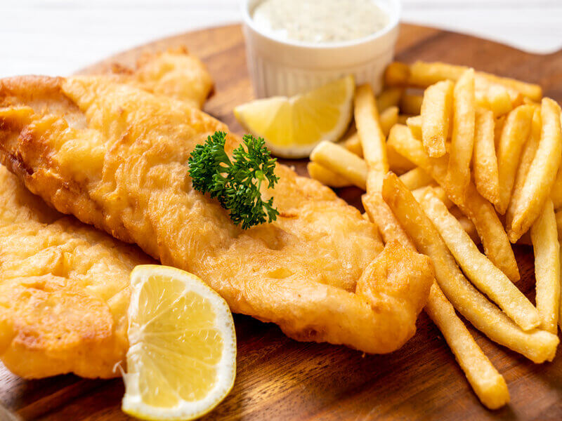 Peixe frito em cima de uma tábua de madeira com batata frita