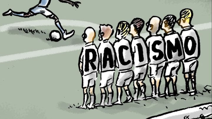 Na imagem o jogador Vini Jr. aparecendo batendo uma falta, com sete jogadores fazendo uma barreira a sua frente. Nas costas de cada um dos sete jogadores tem uma letra que formam a palavra "racismo".