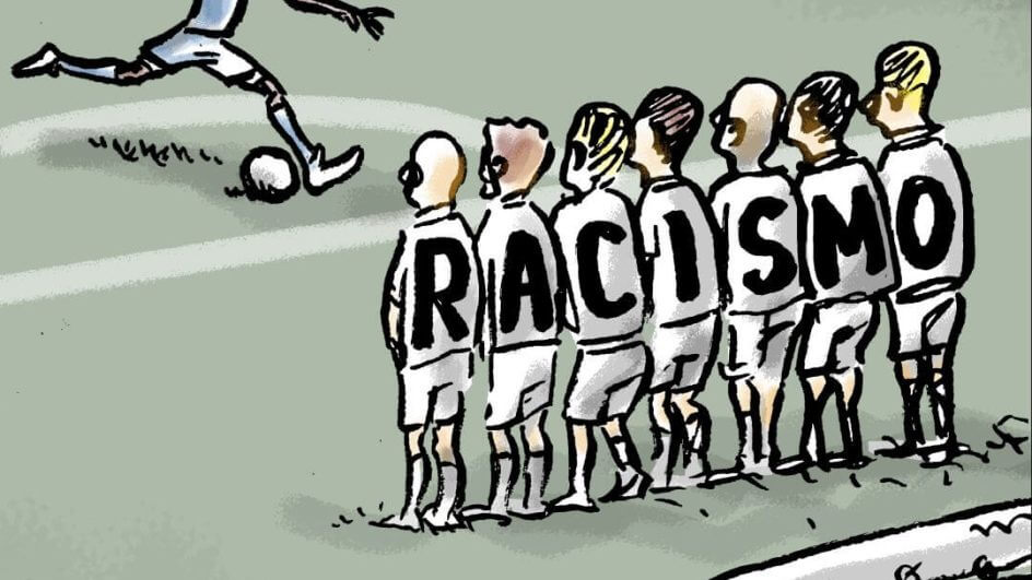 Na imagem o jogador Vini Jr. aparecendo batendo uma falta, com sete jogadores fazendo uma barreira a sua frente. Nas costas de cada um dos sete jogadores tem uma letra que formam a palavra "racismo".