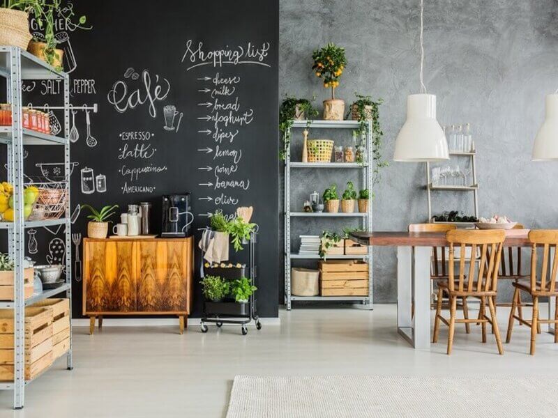 Sala com lousa na parede, móveis de madeira e estante com plantas