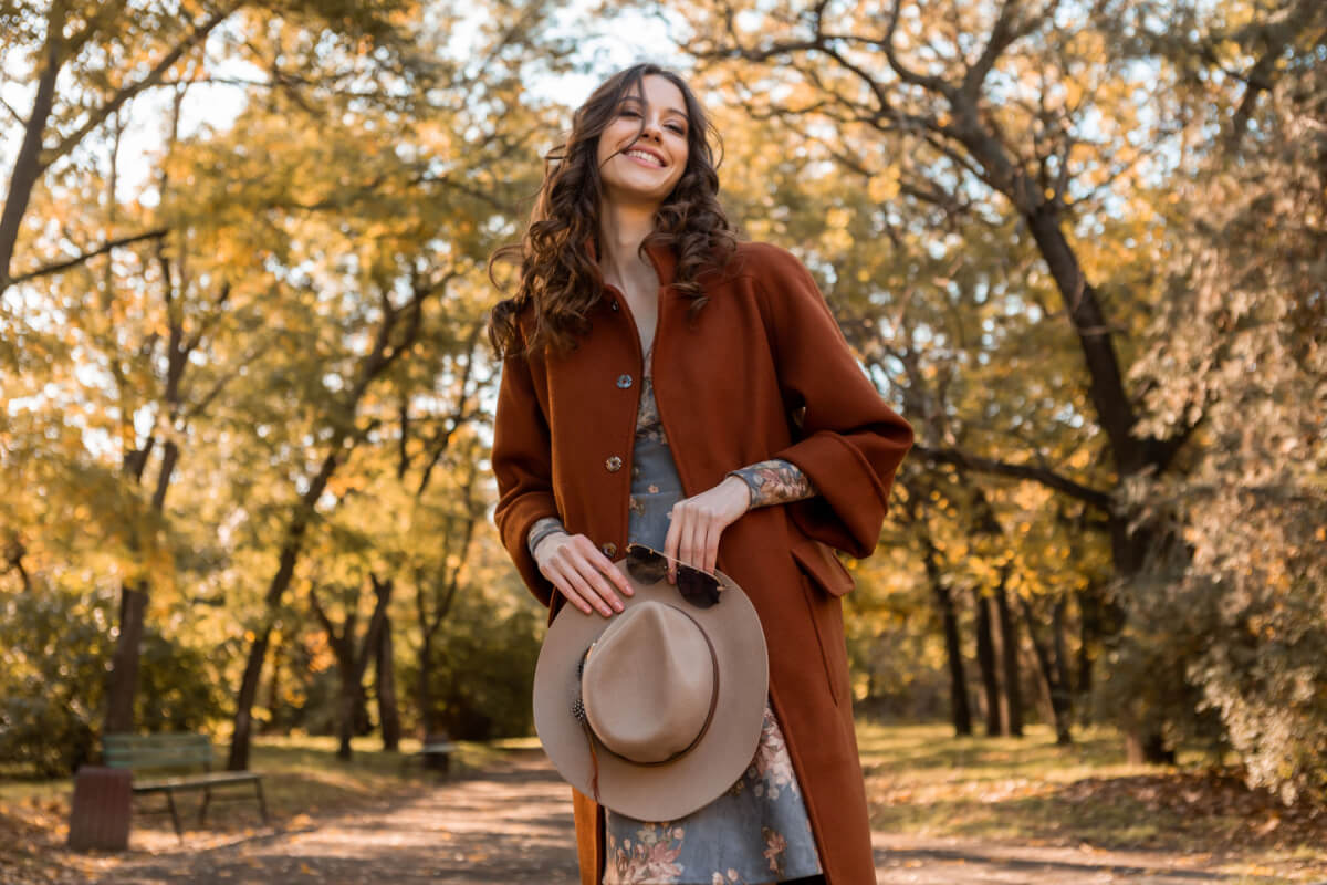 Mulher elegante segurando chapéu, óculos de sol e vestida com um casaco trech coat