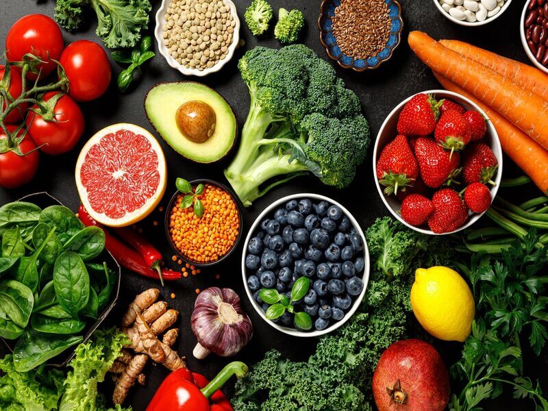 Mesa com brócolis, abacate, laranja, morango e outras frutas espalhadas