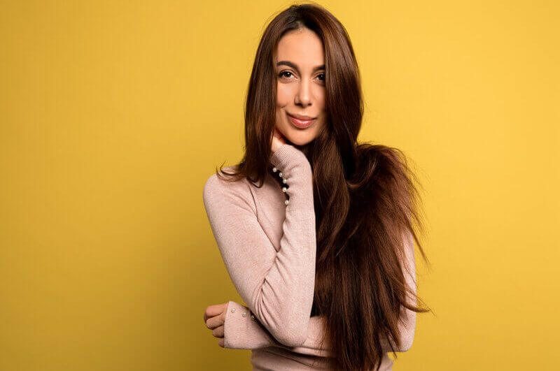 Mulher com cabelos longos usando blusa bege sorrindo em frente a um fundo amarelo