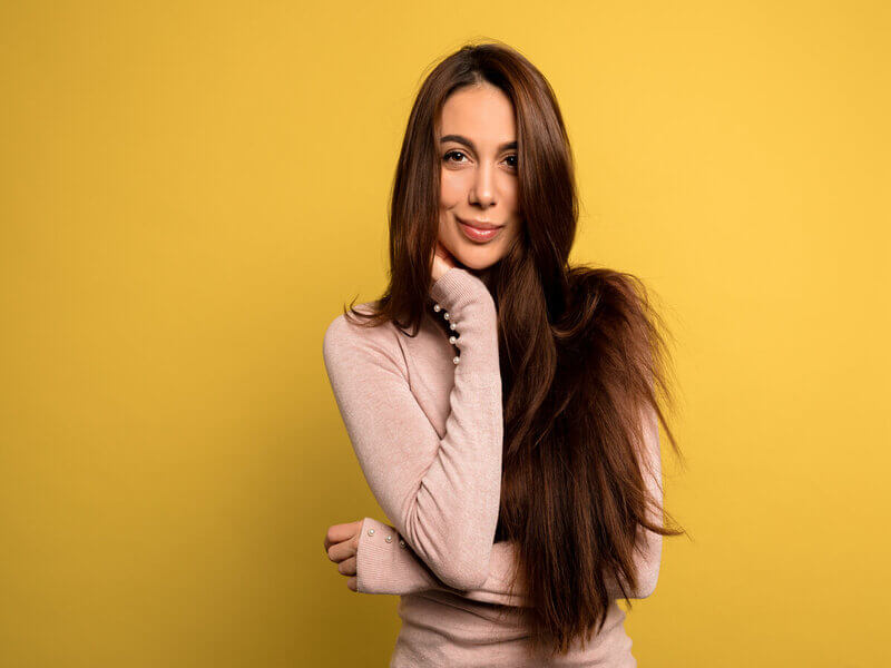 Mulher com cabelos longos usando blusa bege sorrindo em frente a um fundo amarelo