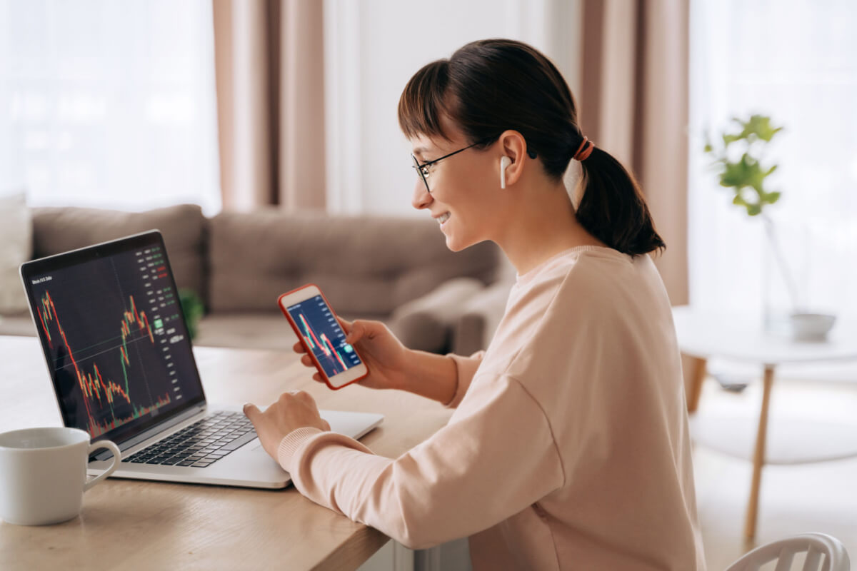 Mulher analisando gráficos financeiros em celular e computador