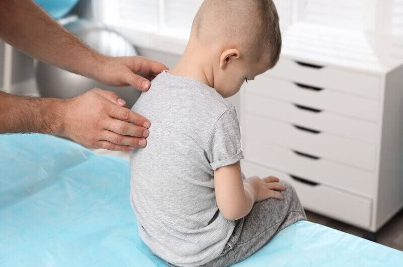 Mãos de adulto examinando costas de criança