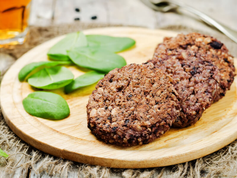 Hambúrguer vegetariano de feijão-preto em tábua com folhas de rúcula
