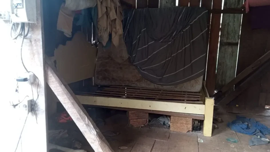 pequeno galpão de madeira com cama e roupas da vitima