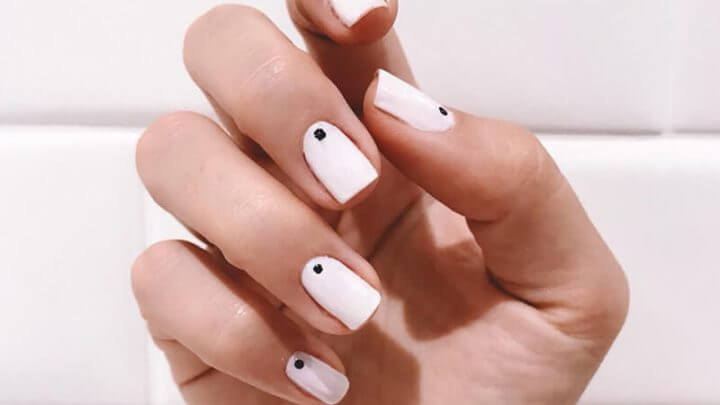 Nail art branca com pingo preto no início do dedo, em mão direita