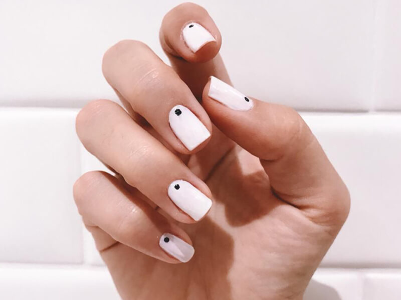 Nail art branca com pingo preto no início do dedo, em mão direita
