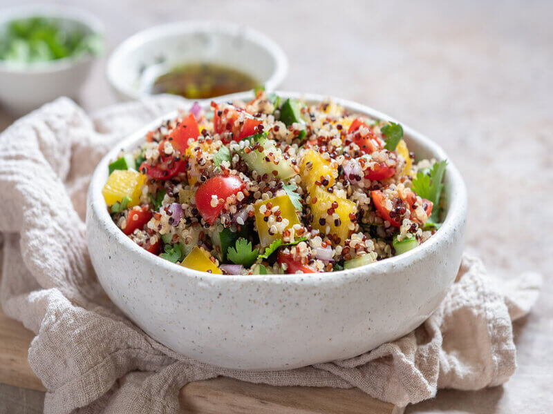 Recipiente branco com quinoa, tomate, pimentão amarelo, pepino e folhas de coentro