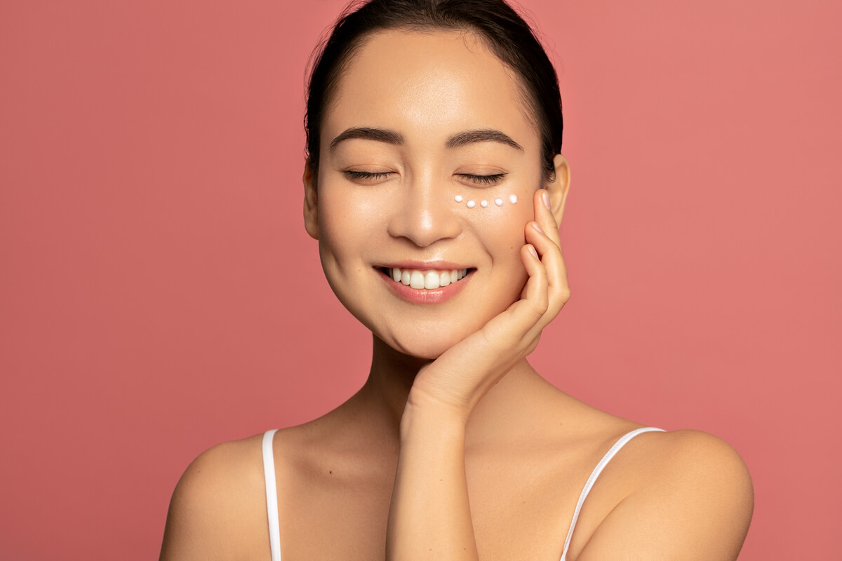 Mulher de olhos fechados e sorrindo com a mão no queixo em fundo coral.