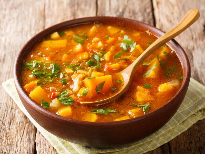 Recipiente marrom com sopa de batata-doce polvilhada com coentro