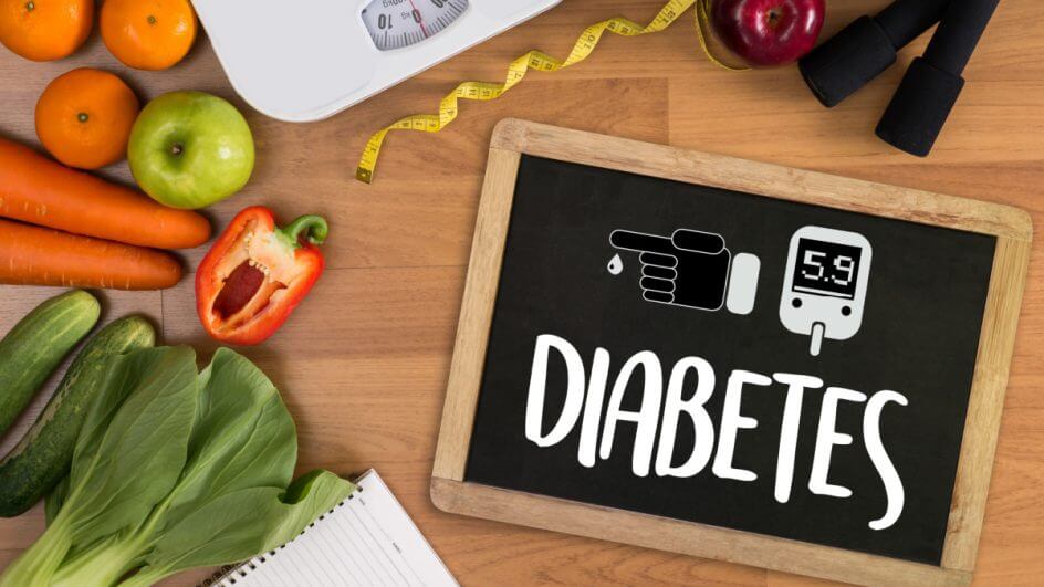 Frutas e legumes, uma balança, uma fita métrica e uma lousa escrito "diabetes" sob mesa de madeira