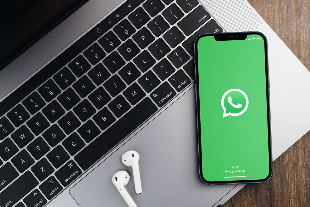 Aplicativo WhatsApp na tela do smartphone em cima de um computador na mesa de madeira