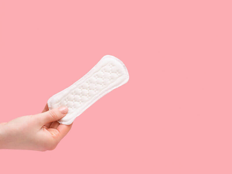 mão segurando absorvente externo em fundo rosa