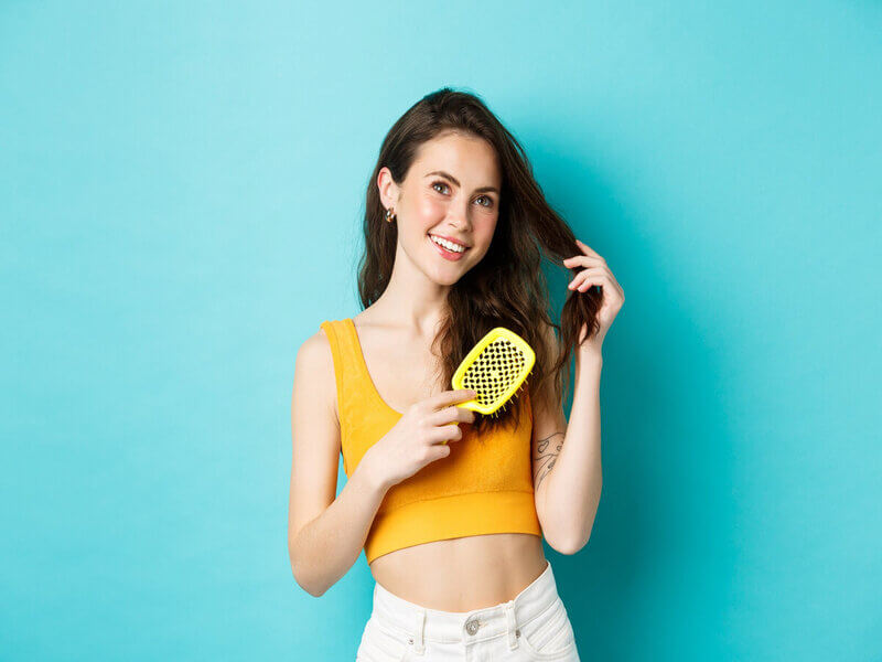 Mulher com blusa amarela penteando os cabelos e sorrindo