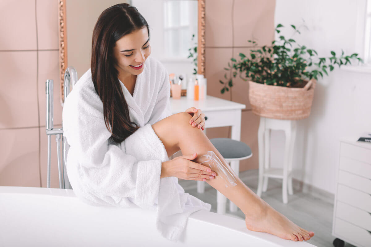 Mulher sentada em um banheiro passando creme nas pernas
