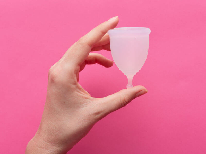 mão segurando coletor menstrual em fundo rosa