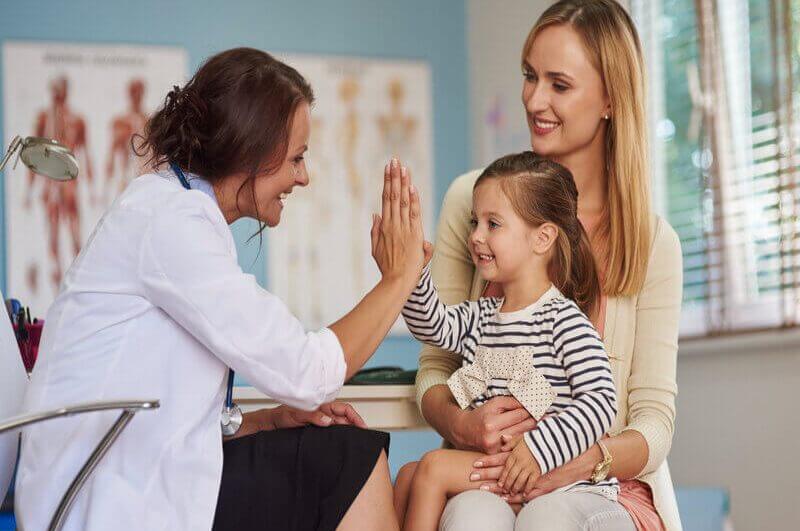 Médica fazendo high five com uma menina sentada no colo de outra mulher
