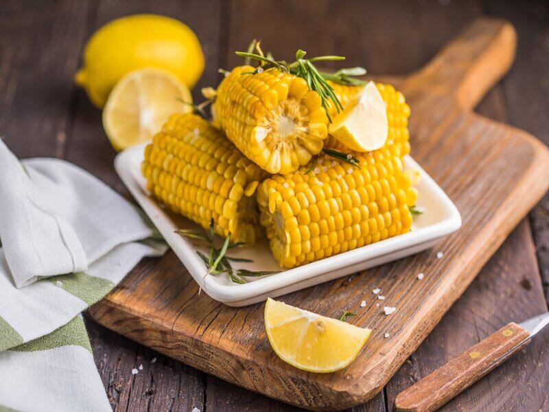 Prato branco com espigas de milho empilhadas em cima de uma tábua de madeira