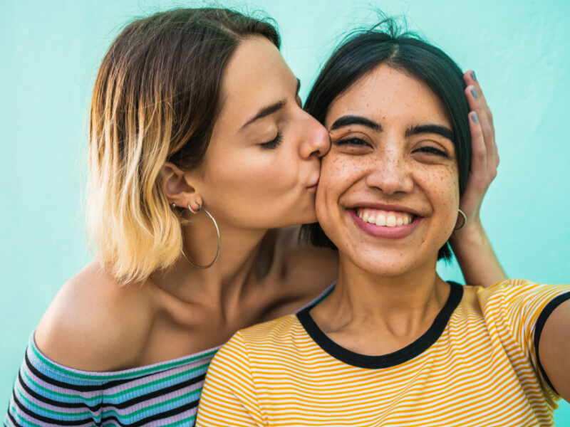Mulher loira beijando bochecha de mulher morena