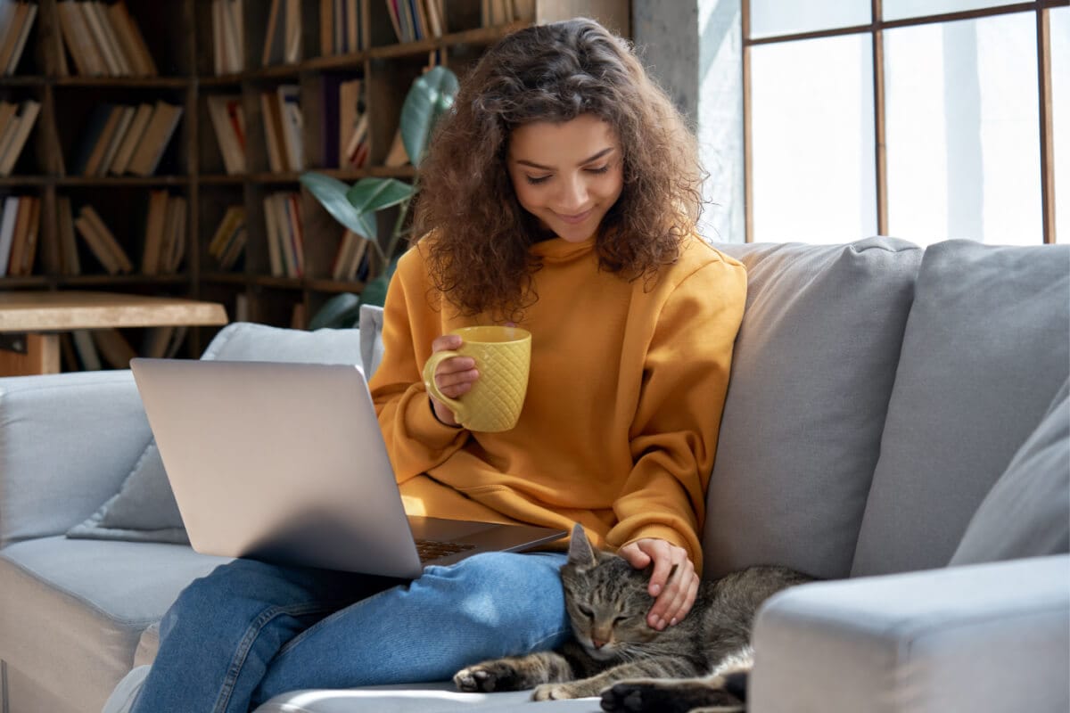 Mulher com notebook no colo fazendo carinho na cabeça do gato