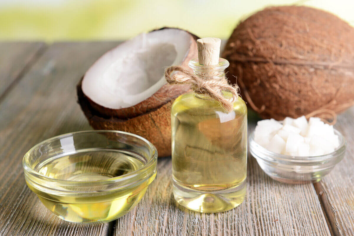 Recipientes de vidro com óleo e pedaços de coco ao fundo em cima de uma mesa de madeira