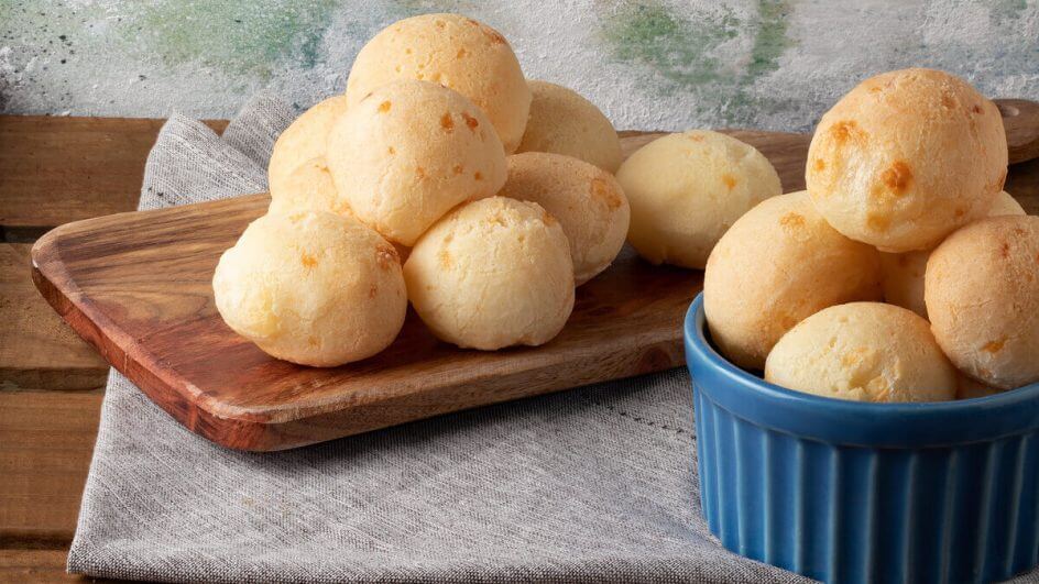 Pães de queijo em tábua de madeira e pote azul