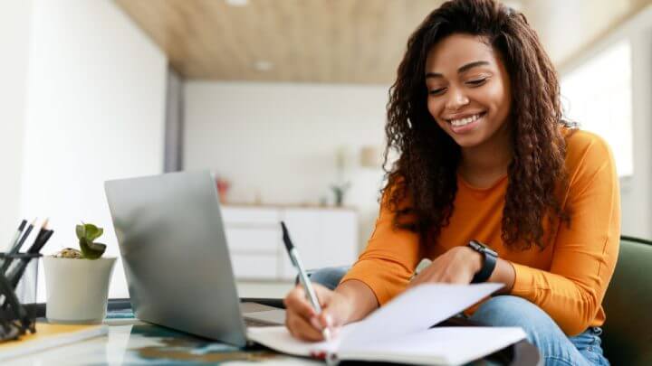 Mulher estudando e fazendo anotações em frente ao notebook
